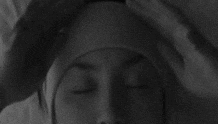 Video gif. Woman is lying in bed wearing a headband pulls it down over her eyes, revealing the message "let me sleep."