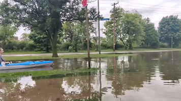 Woman Kayaks Along Flooded Street 