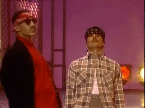 TV gif. Next to a stage with blinking stage lights, two men on Soul Train stand stiffly and nod, then shake their heads in a strange synchronized dance.