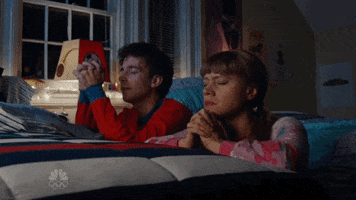 SNL gif. Kate McKinnon and Kyle Mooney kneel at a bed with their hands folded and eyes closed, praying.