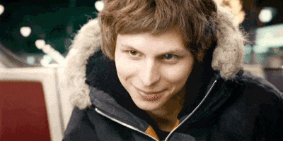 Celebrity gif. With fireworks exploding in the background, Michael Cera smiles at us and winks.
