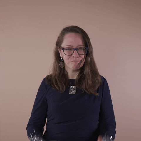 Reaction gif. A Disabled Latina woman with brown wavy hair and glasses slow claps with an articulate nod and enigmatic smirk.