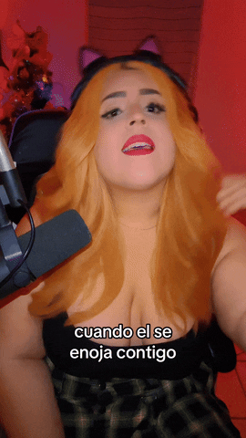 Video gif. Shalymar Rivera Gonzalez wears cat ear headphones and a strawberry blonde wig. She gently flips her hair confidently with her chin turned upwards. Text reads, "Cuando se enoja contigo."