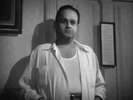 Movie gif. Dan Seymour as Angel in Key Largo stands near a wall, hands in his white jacket pockets, shrugging his shoulders indifferently and saying "sorry," which appears as text.