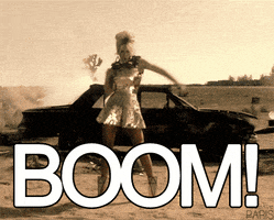 Music video gif. From Beyonce's "Run the World," Beyonce wears a sparkling dress and strikes a pose with her fist in the air, right as an old car behind her explodes. Text, "Boom!"
