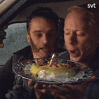 TV gif. Peter Settman and Fredde Granberg as Ronny and Ragge. They're sitting in a car and are holding a plate with a cake and a burning candle. They stare at the cake before blowing it out and squirming in glee.  