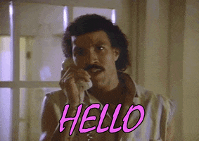 Music video gif. Lionel Richie, phone to his ear, sings “HELLO” to us.