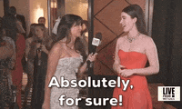 Met Gala 2024 gif. Nell Diamond smiles and responds to an interview question, saying "Absolutely, for sure!" Her hair is swept behind her ears and worn straight down her upper back. She's wearing a cherry red Hill House Home sleeveless gown with a sheer flowing skirt.