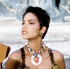 Movie gif. Halle Berry as Sharon Stone in "The Flintstones" looks up and gives a slow seductive blink.