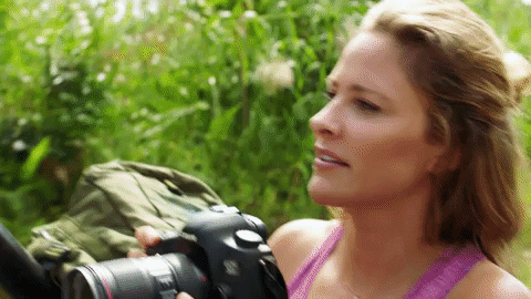 A woman is taking pictures of a green landscape filled with trees and natural scenery.