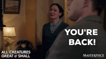 TV gif. Anna Madeley as Mrs. Hall on All Creatures Great and Small walks up to a man with a big, warm smile on her face. She says, “You're back!” and gives him a big hug.
