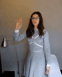 Video gif. We follow a hand as it high-fives a woman in a gray dress with pointy blue-rimmed glasses.