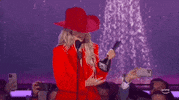 ACM Awards gif. Country artist Lainey Wilson looks at award in hand, gleefully laughs, and spins the bottom of the thropy with one hand.