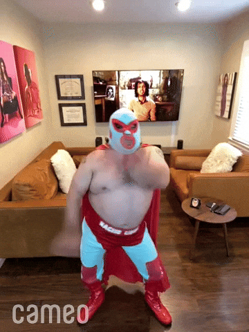 Video gif. Phone video of a man dressed in a Nacho Libre costume dances in his living room for us, his arms windmilling around.