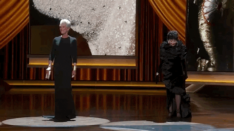 Oscars 2024 gif. We pan across the stage as Rita Moreno, Jamie Lee Curtis, Lupita Nyong'o, and Mary Steenburgen emerge underneath the spotlight. 