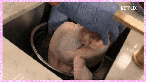 Reality TV gif. With a grimace Paris Hilton on Cooking with Paris tries to stuff a raw, whole turkey into a pot. Text, "Ooh, oh my god."