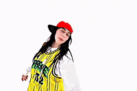Music Video gif. From Billie Eilish's music video for "LUNCH", Billie is on a stark white background dressed in a white long sleeve shirt and a yellow and black jersey over the top, with a red flat brim hat on. She is clapping and turning around while looking at the camera.