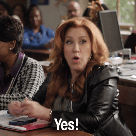 TV gif. Lisa Ann Walter as Melissa in Abbott Elementary. She's sitting in a classroom squeezing her hands into fists and her eyes are wide as she bursts into excitement on loop. Text, "Yes!"