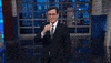 TV gif. Stephen Colbert as host of The Late Show steps toward us as he does the sign of the cross and then a chef's kiss before looking upward.