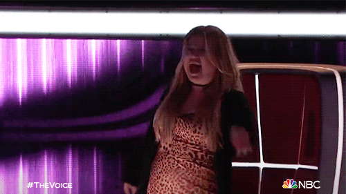 Reality TV gif. Kelly Clarkson on "The Voice" standing up from her judge seat and dancing during a performance.
