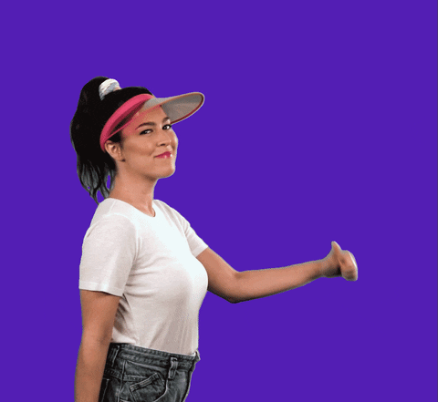 Video gif. A person wearing a pink visor dances and points at themself with their thumbs. Words appear in front of them that say, “we're here, we're queer, get used to it."