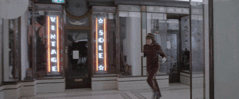 Music video gif. From the video for Elevator Operator, Courtney Barnett dressed in a red uniform runs through an art-deco hallway toward a set of elevators.