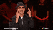 Reality TV gif. Howie Mandel on America's Got Talent crossing his fingers with both hands and bowing his head, praying for luck.
