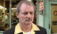 Movie gif. Bill Murray as Herman Blume in Rushmore stands outside a barber shop, unmoving, staring into the distance deep in thought.