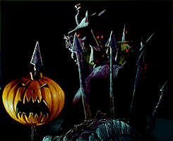 Movie gif. In a scene from The Nightmare Before Christmas, we slowly zoom in toward a spooky mansion as falling jack o lanterns become shish kabobs on sharp metal fence posts.