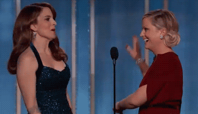 Celebrity gif. Amy Poehler and Tina Fey stand on stage at the Golden Globes. They look at each other while they laugh and give each other a big high five like they know they just said a hilarious joke.