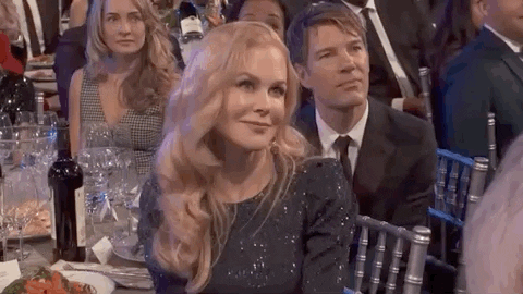 Celebrity gif. Nicole Kidman sits at a table at the 2020 SAG Awards smiles and shrugs her shoulders.