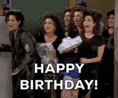 Friends gif. Seven women with similar hairstyles and outfits burst into the apartment holding gifts and shouting "Happy Birthday!" which appears as text.