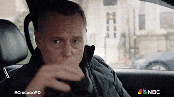 TV gif. Jason Beghe as Hank in Chicago PD, seated in his car, peers out of the window with binoculars.