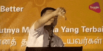 Video gif. Man stands at a podium and he angrily shoves a big thumbs down towards the crowd as he says, “Boo” into the microphone.