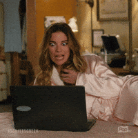 Schitt's Creek gif. Annie Murphy as Alexis lounges in a robe on a bed in front of an open laptop. She looks at the laptop, her eyes widening comically, twists her hair in her hand and says what appears as text, "Yum!"