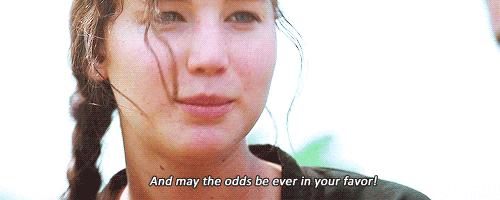 Movie gif. Jennifer Lawrence as Katniss in The Hunger Games looks over at Gale and eats a piece of bread after she says with a sarcastic smile, “And may the odds be ever in your favor!”
