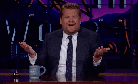 TV gif. Sitting at his desk, James Corden of The Late Late Show holds his hands up in confusion and squints, looking around as if to say, “What?”