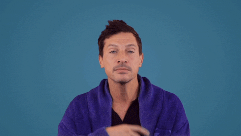 Celebrity gif. Wearing a blue zip up sweater against a lighter blue background, a pensive Simon Rex holds a hand to his chin, and nods as if he's mulling over some info.
