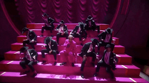 Oscars 2024 GIF. Ryan Gosling is performing I'm Just Ken and he sits on steps with his male posse, all of them holding a champagne glass. They raise their glasses in unison, whip it down to break it, and end with stabbing themselves with the faux broken glass. 