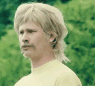 Music video gif. Tom DeLonge of Blink 182 in the First Date music video wears a blonde mullet wig. He looks around with a super concerned expression on his face and says, “What the fuck?”