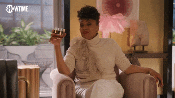 TV gif. Jenifer Lewis as Patricia in I Love That For You leans forward from her armchair holding a glass and saying "cheers, baby" which appears as text.
