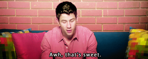 Celebrity gif. Nick Jonas leans forward on a couch and looks at us, saying, “Awh, that’s sweet.”