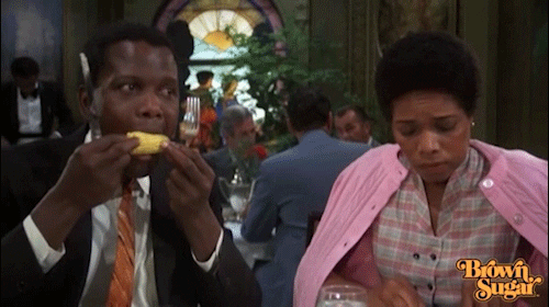 Movie gif. Sidney Poitier, as [TK] in [TK], holds a knife and fork in each hand as he chomps on a corn cob, and his female dining companion glances at him with a worried look as she cuts her food.