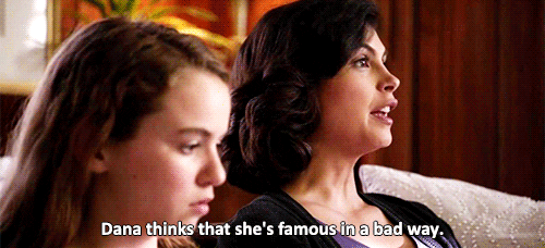 TV gif. Morena Baccarin as Jessica on Homeland sits on a white couch next to a girl in the foreground. She says glibly as the girl turns to look at her, "Dana thinks that she's famous in a bad way."