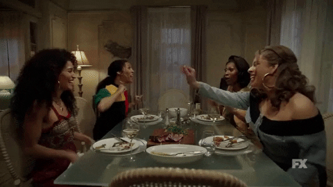 TV gif. The girls from Pose are sitting at a dining table and they all chat enthusiastically while laughing and high fiving one another.