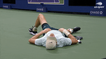 Sports gif. Jannik Sinner from the 2023 US Open lays on the ground with his racket next to him. He has his hands on his stomach and is breathing heavily.