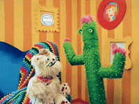 TV gif. A cactus puppet with pink flowers talks to Scruffy, a white fluffy dog puppet in Happy Place, wearing a tiny cowboy hat, saying, "Well, thank you!" on a brightly-colored cartoon-style living room set.