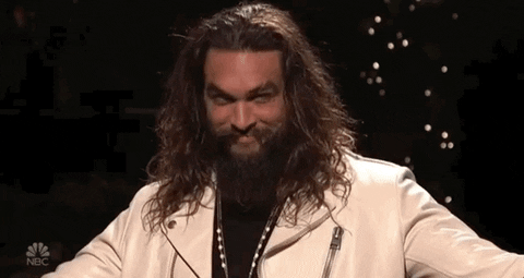 SNL gif. Jason Momoa smiles devilishly while looking around and holding out his arms.