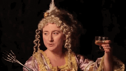 Music video gif. A woman in Radical Face's We're On Our Way wears a powdered wig and ball gown as she toasts her glass with a look of resolve before drinking. 