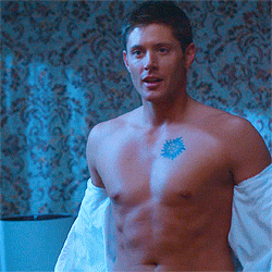 TV gif. Jenson Ackles as Dean in Supernatural seductively removes his white shirt.